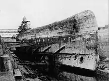 A large ship upside-down and braced in a drydock