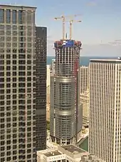 a tall skyscraper under construction in the middle of a city viewed from an elevation of about 40 stories in another building