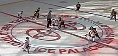 Adolescent boys playing ice hockey, depicting a face off with a referee dropping a puck