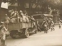 Several dozen soldiers disembark from two trucks.