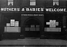 Building with the words "The Mothers' and Babies' Welcome" in large white capital letters, above the door and windows