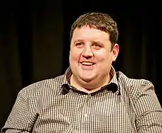 A laughing, dark-haired man in a chequered shirt