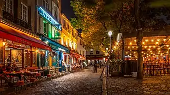 A street in the evening lined with several open-air cafes.