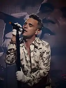 Photograph of Robbie Williams singing into a microphone while closing his eyes