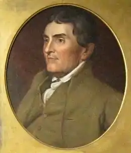 Portrait shows a clean-shaven man with dark brown hair wearing a brown coat over a white shirt.